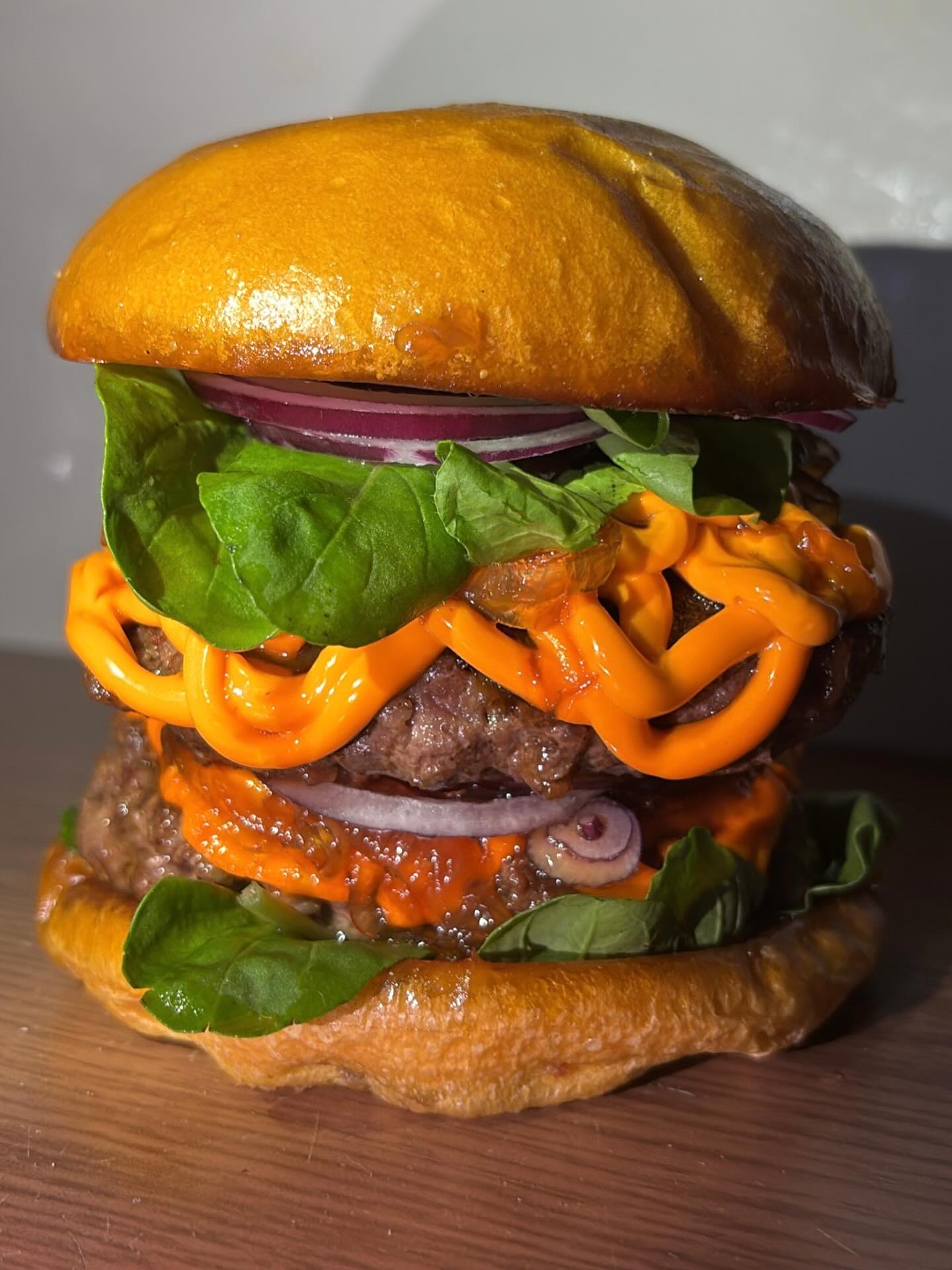 Hambúrguer artesanal duplo com molho cheddar, cebola roxa e folhas frescas